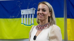 Марлейн Маас в укритті біля прапора України з зображенням карти Херсонської області і стели на в’їзді до міста