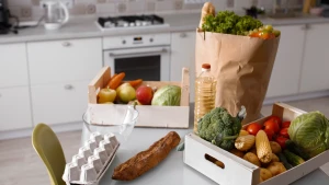 Кошик продуктів із свіжими товарами, крупами та побутовими покупками на кухонному столі під час вигідних закупів