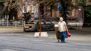 Прифронтовий Херсон: щоденне життя між руїнами. Жінка перетинає вулицю повз обвуглений кістяк автівки. Фото Олександра Андрющенка / «Вгору» 
