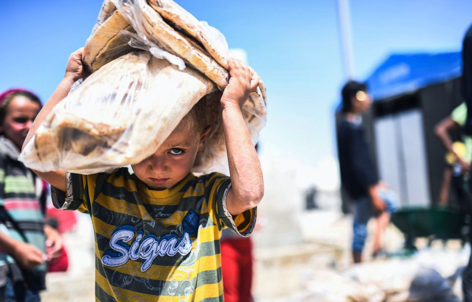 Cирійська дитина несе хліб у тимчасовому таборі в селі Айн-Ісса 11 липня 2017 року. (Photo by Bulent Kilic / AFP Photo)